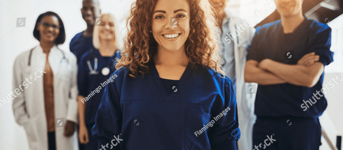 stock-photo-smiling-young-female-doctor-standing-in-a-hospital-corridor-with-a-diverse-group-of-medical-staff-1208448841